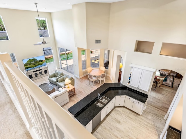 living room featuring light wood-style floors, arched walkways, a towering ceiling, a ceiling fan, and baseboards