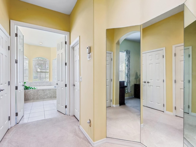 hallway featuring arched walkways, light colored carpet, baseboards, and light tile patterned flooring