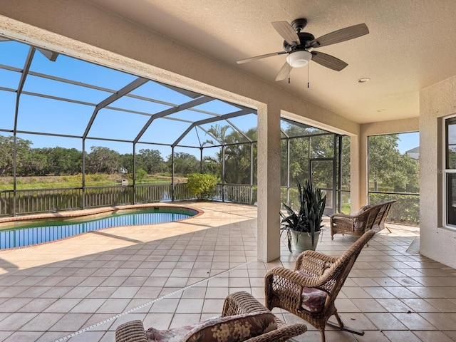 view of swimming pool with a ceiling fan, a patio, view of scattered trees, and a lanai