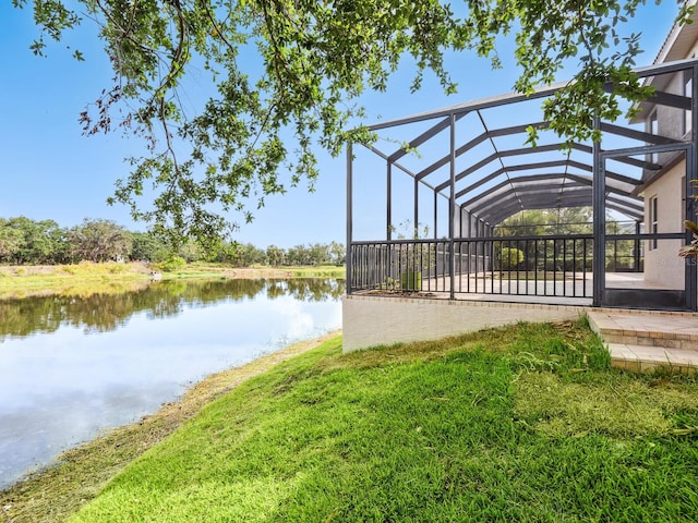 dock area with a water view, glass enclosure, a patio, and a lawn