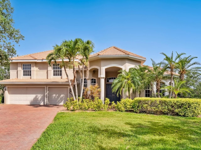 mediterranean / spanish house featuring a front lawn, decorative driveway, stucco siding, a garage, and a tile roof