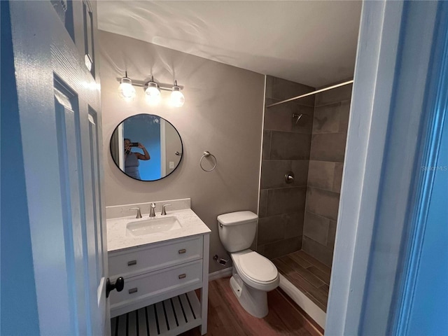 bathroom featuring toilet, vanity, tiled shower, and wood finished floors