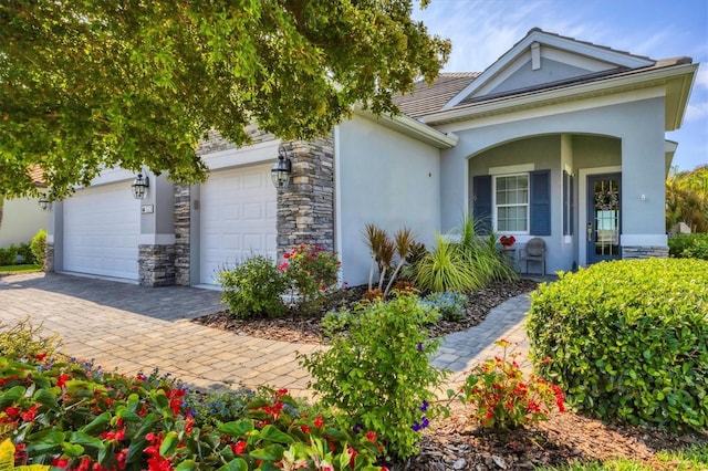 view of home's exterior featuring stucco siding, decorative driveway, stone siding, an attached garage, and covered porch