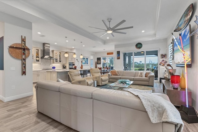 living room featuring a tray ceiling, a ceiling fan, light wood-type flooring, recessed lighting, and baseboards