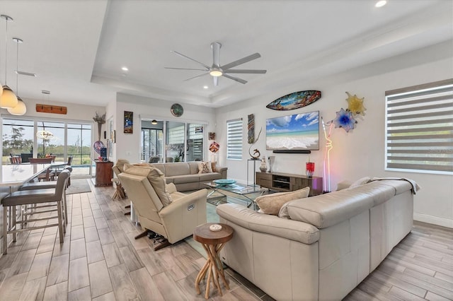 living area featuring a raised ceiling, a ceiling fan, light wood-style flooring, recessed lighting, and baseboards