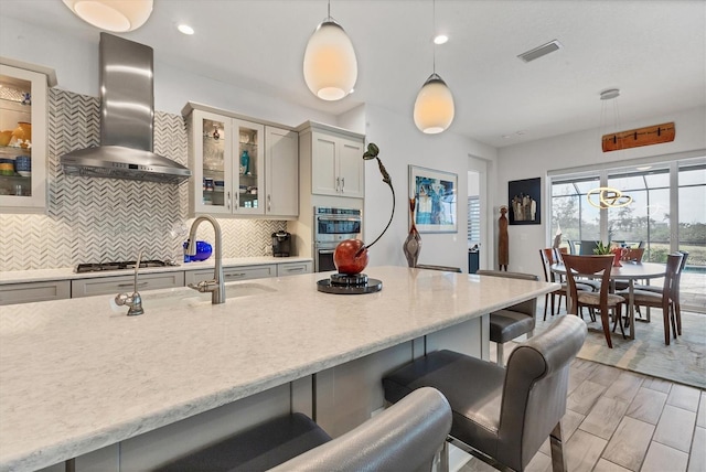 kitchen featuring wall chimney range hood, stainless steel appliances, a breakfast bar area, tasteful backsplash, and hanging light fixtures