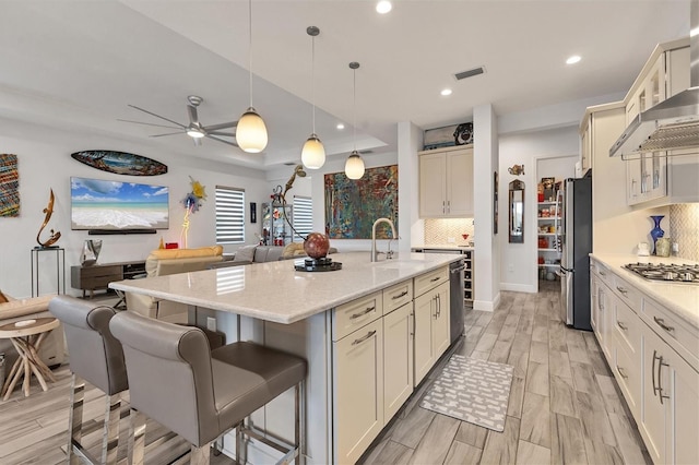 kitchen with appliances with stainless steel finishes, a sink, decorative backsplash, a breakfast bar, and light wood-type flooring