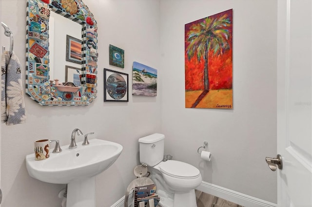 half bath featuring toilet, baseboards, and a sink