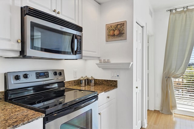 kitchen with appliances with stainless steel finishes, white cabinets, and dark stone counters
