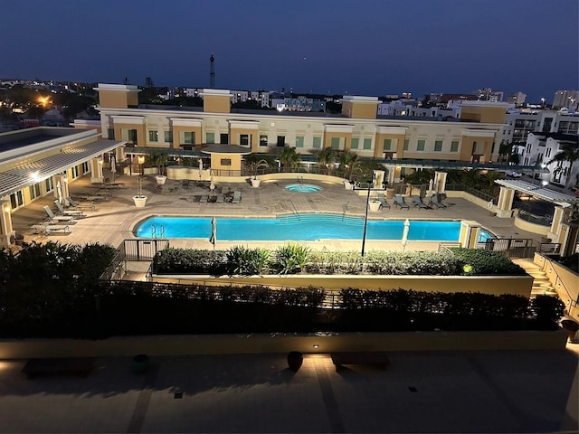 pool at night featuring a patio area and a community pool