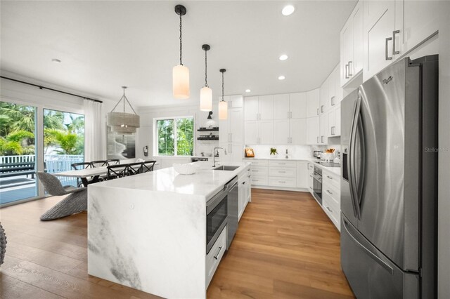 120 White Ave, Anna Maria, FL 34216 - kitchen featuring appliances with stainless steel finishes, light wood-type flooring, a sink, white cabinetry, and decorative light fixtures