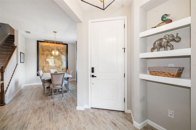 entryway with stairway, light wood-style floors, baseboards, and a chandelier