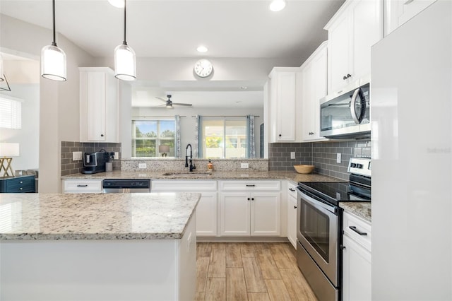 kitchen featuring appliances with stainless steel finishes, a sink, light wood-type flooring, a ceiling fan, and backsplash