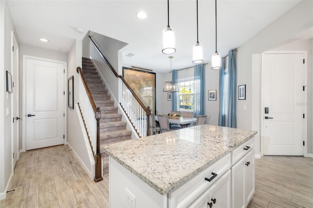 kitchen with light wood-type flooring, a kitchen island, white cabinets, light stone counters, and recessed lighting