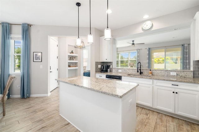 kitchen featuring a sink, light wood-style floors, tasteful backsplash, stainless steel dishwasher, and a kitchen island