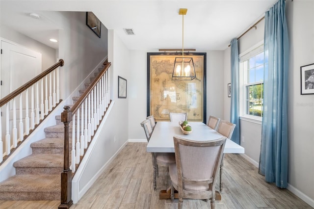 dining room featuring baseboards, stairs, light wood finished floors, and a chandelier