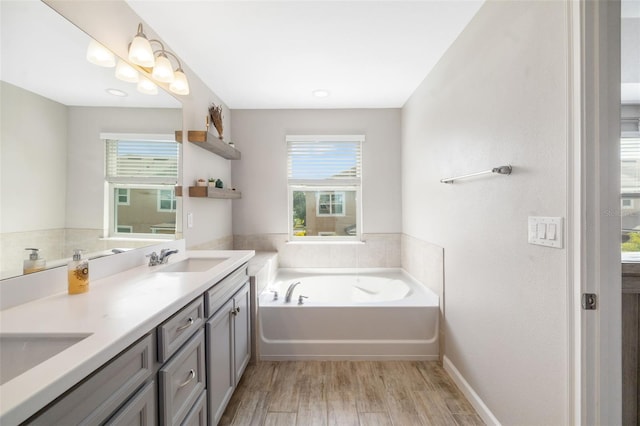 full bathroom with wood finished floors, a garden tub, double vanity, and baseboards