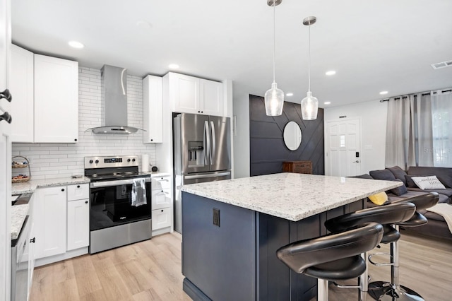 3303 32nd St W, Bradenton, FL 34205 - kitchen featuring stainless steel appliances, wall chimney exhaust hood, light wood finished floors, a kitchen island, and a breakfast bar area