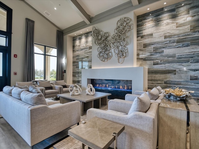 living area with a glass covered fireplace, an accent wall, high vaulted ceiling, and beamed ceiling