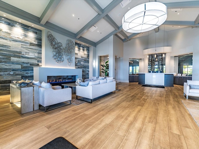 living area featuring beamed ceiling, wood finished floors, high vaulted ceiling, a glass covered fireplace, and an accent wall