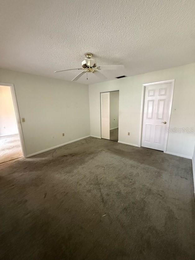 1304 56th St W Unit 1304, Bradenton, FL 34209 - unfurnished bedroom with baseboards, a textured ceiling, a closet, dark carpet, and a ceiling fan