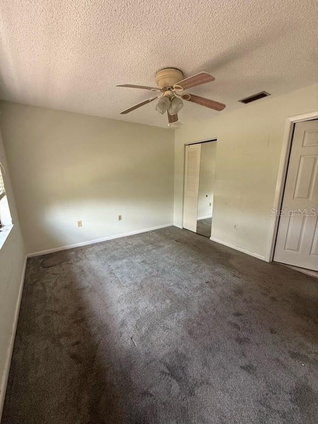 1304 56th St W Unit 1304, Bradenton, FL 34209 - unfurnished bedroom featuring a textured ceiling, dark carpet, baseboards, and a ceiling fan