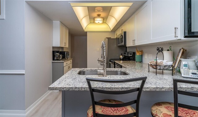 4621 Gulf Of Mexico Dr Unit 2F, Longboat Key, FL 34228 - kitchen featuring stainless steel appliances, light stone countertops, white cabinets, light wood-style floors, and a peninsula