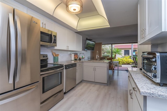 4621 Gulf Of Mexico Dr Unit 2F, Longboat Key, FL 34228 - kitchen with appliances with stainless steel finishes, a peninsula, light wood-style floors, light stone countertops, and white cabinetry