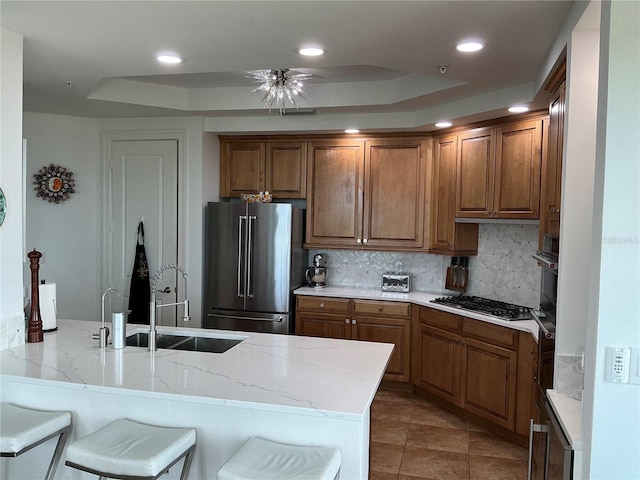 130 Riviera Dunes Way Unit 304, Palmetto, FL 34221 - kitchen with appliances with stainless steel finishes, a tray ceiling, brown cabinets, backsplash, and light stone counters