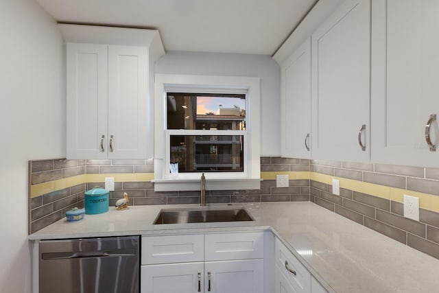 kitchen with stainless steel dishwasher, a sink, light countertops, white cabinetry, and backsplash