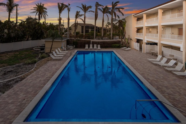 pool at dusk with a patio, fence, and a community pool