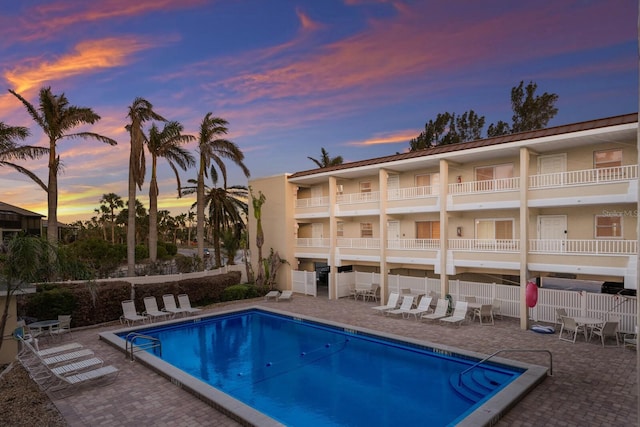 pool at dusk featuring a community pool, a patio area, and fence