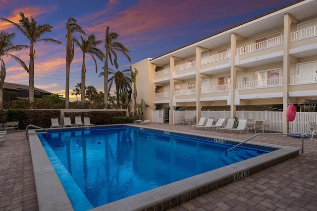 pool at dusk featuring fence, a community pool, and a patio area