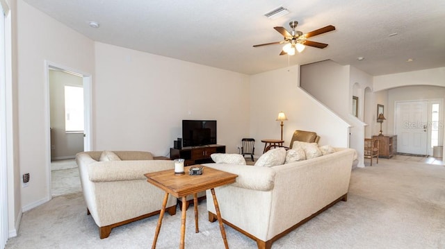 living area with light carpet, arched walkways, ceiling fan, and baseboards