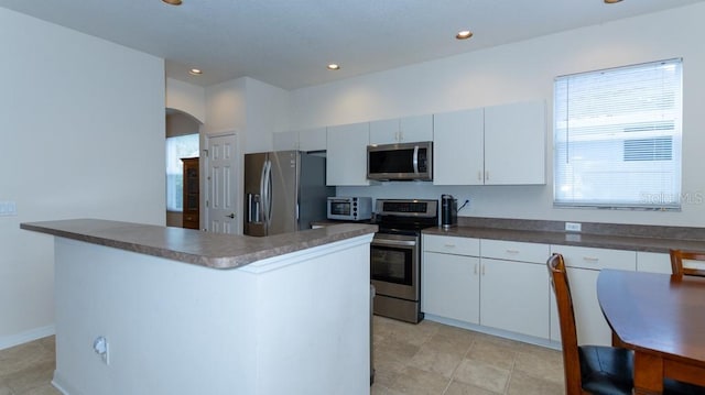 kitchen with appliances with stainless steel finishes, arched walkways, dark countertops, recessed lighting, and white cabinets
