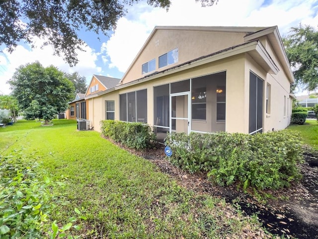 rear view of property featuring stucco siding, a lawn, a sunroom, and central air condition unit