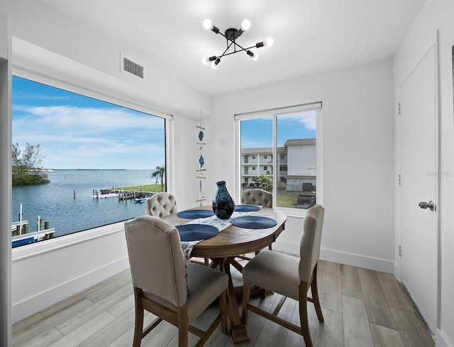 dining area with a chandelier, light wood finished floors, a water view, and baseboards