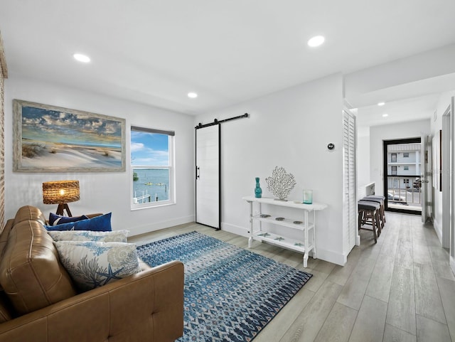 living room with a barn door, light wood finished floors, recessed lighting, and baseboards