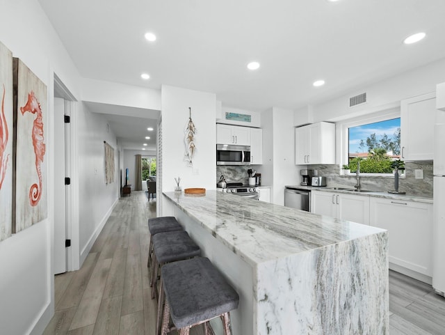 kitchen with stainless steel appliances, light stone counters, backsplash, white cabinetry, and recessed lighting