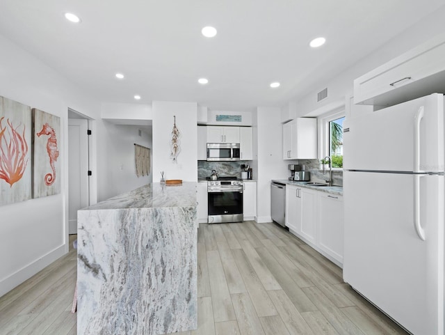 kitchen featuring stainless steel appliances, a sink, white cabinetry, light stone countertops, and tasteful backsplash