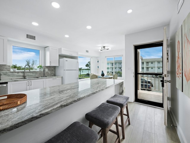 kitchen with a sink, freestanding refrigerator, a kitchen bar, light stone counters, and recessed lighting