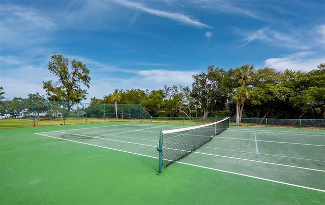 view of tennis court featuring fence, community basketball court, and view of wooded area