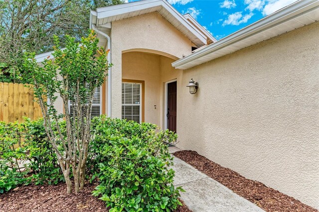 entrance to property featuring stucco siding and fence