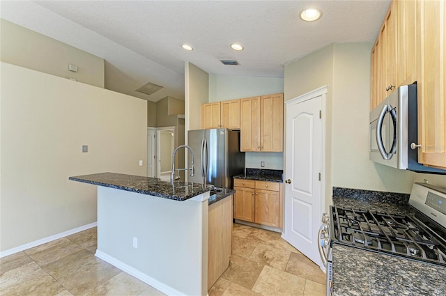 kitchen featuring stainless steel appliances, lofted ceiling, light brown cabinets, dark stone counters, and a center island with sink