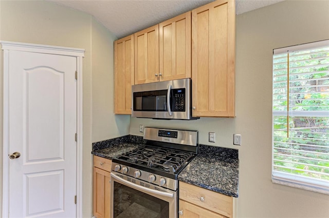 kitchen with appliances with stainless steel finishes, light brown cabinetry, plenty of natural light, and a textured ceiling