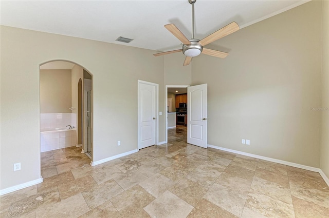 unfurnished bedroom with arched walkways, baseboards, light stone finish floors, ensuite bath, and vaulted ceiling