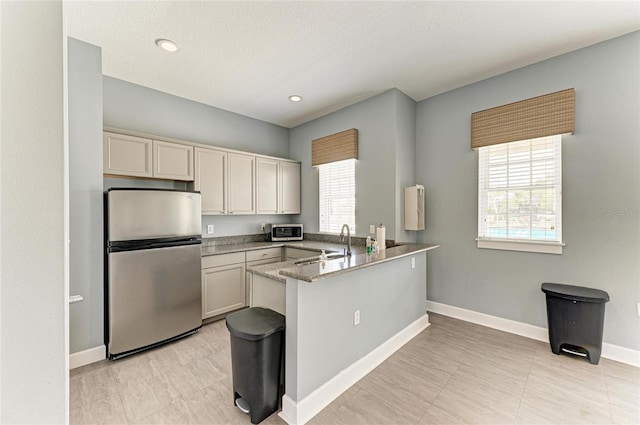 kitchen with appliances with stainless steel finishes, baseboards, a peninsula, a sink, and light tile patterned floors