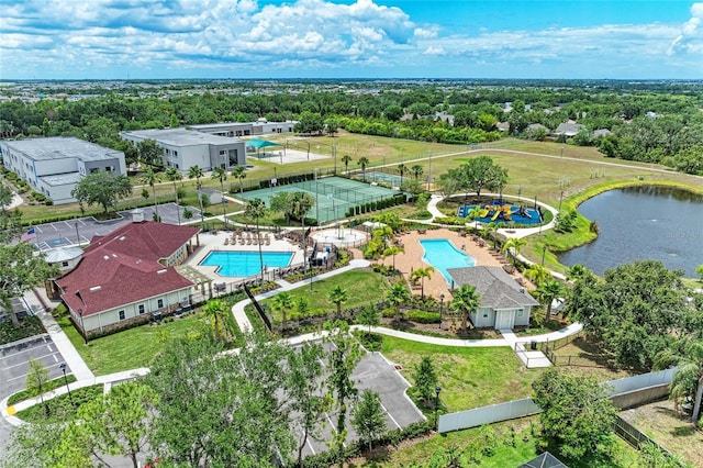 aerial view of a pool area, a nearby body of water, and a tree filled landscape