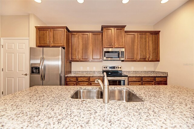 12091 Firewheel Pl, Venice, FL 34293 - kitchen with appliances with stainless steel finishes, a sink, brown cabinetry, recessed lighting, and light stone counters