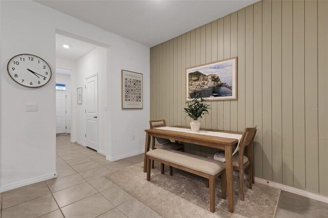 dining room featuring light tile patterned flooring, baseboards, and wooden walls